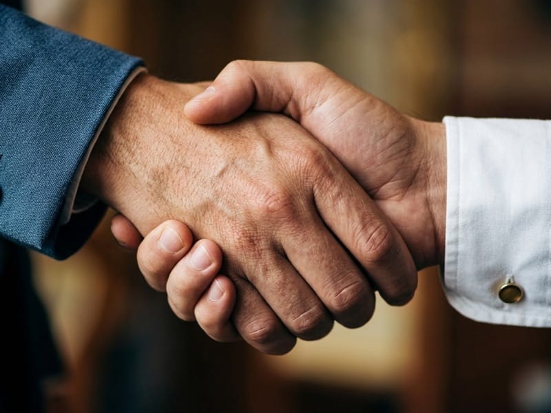 Two men shaking hands, one in a blue jacket and one in a white shirt