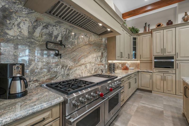 Chef's kitchen with a professional gas range, full-height granite backsplash, and custom light-stained cabinetry