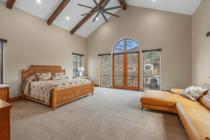 Primary bedroom suite with a vaulted wood-beam ceiling and arched French doors opening onto a balcony