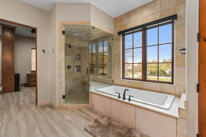Primary bathroom with a walk-in glass shower and a tiled soaking tub beneath a large window